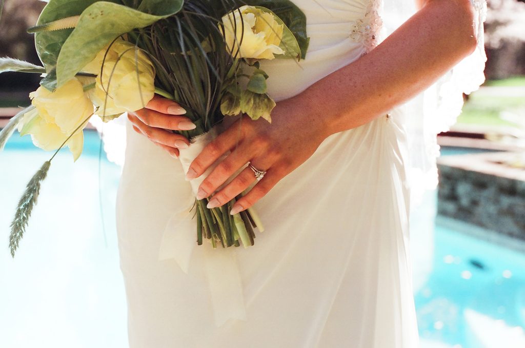 Bride holding a yellow and green bouquet beside the pool at Lakewold Gardens, photographed on CineStill 400D film.
