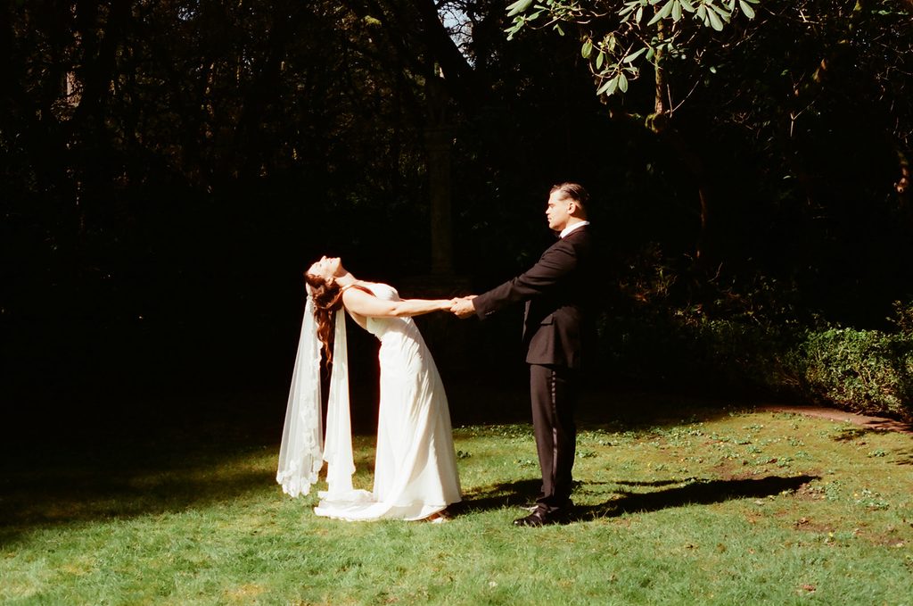 Bride and groom holding hands in dramatic sunlight and shadow on a lawn at Lakewold Gardens, photographed on CineStill 400D film.