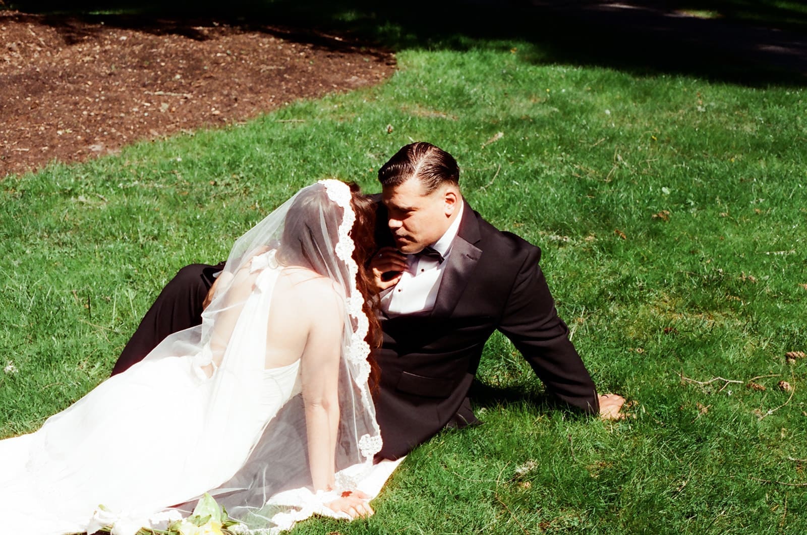Bride and groom sitting together on the grass in bright sunlight at Lakewold Gardens, photographed on CineStill 400D film.