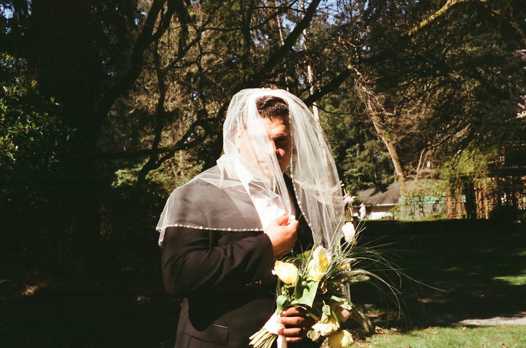 Groom holding a yellow and green bouquet beneath the bride’s veil at Lakewold Gardens, photographed on CineStill 400D film.
