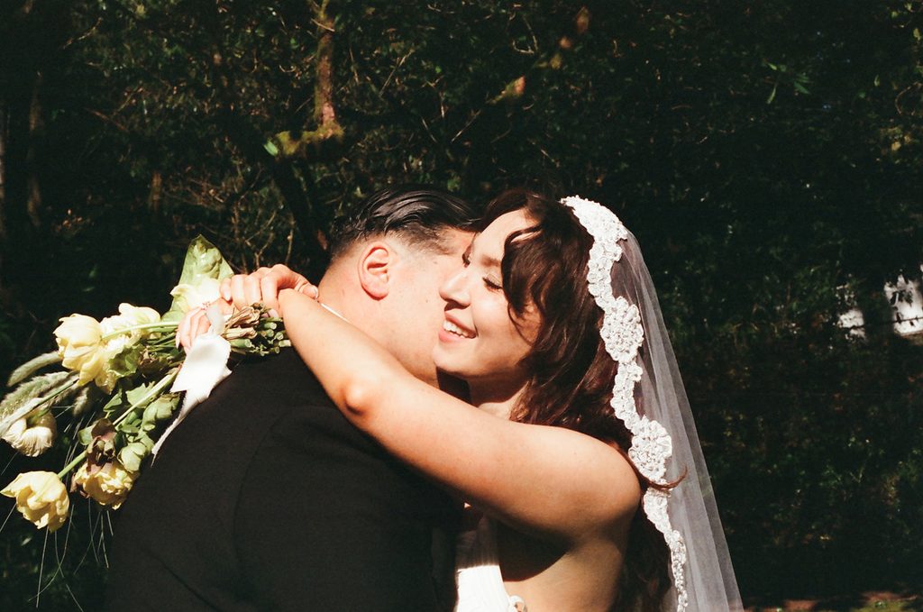 Bride smiling as she hugs the groom with her bouquet over his shoulder at Lakewold Gardens, photographed on CineStill 400D film.