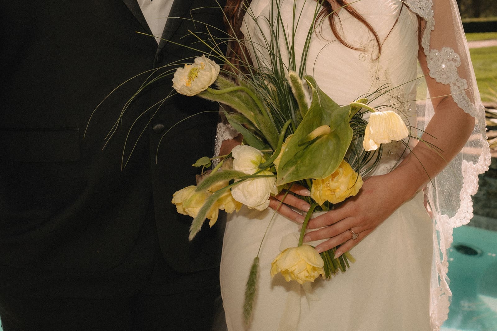 Close up shot of a groom and bride holding a yellow wedding bouquet in front of the pool at Lakewold Gardens. 