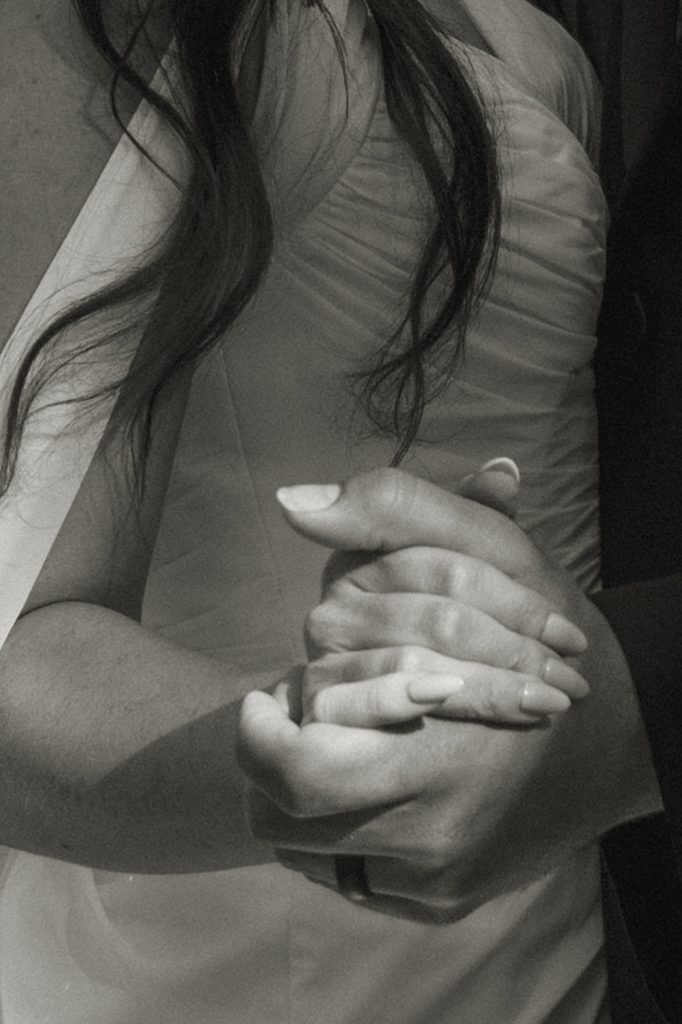 Close up photo of a bride and groom holding hands.