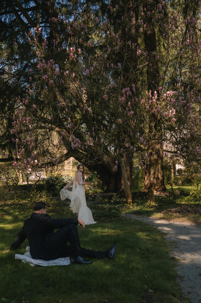 Groom sitting in the grass and watching his bride run around during their Lakewold Gardens wedding photos.