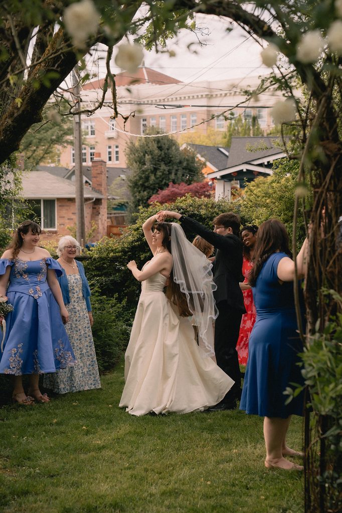 Groom twirling the bride as they dance outdoors surrounded by friends and family.