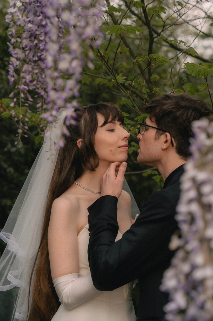 Bride and groom posing near lilac flowers.