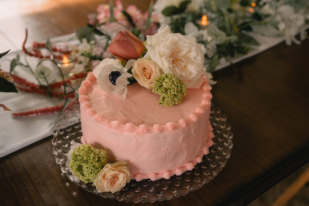 Pink wedding cake decorated with fresh roses and green flowers at an intimate reception