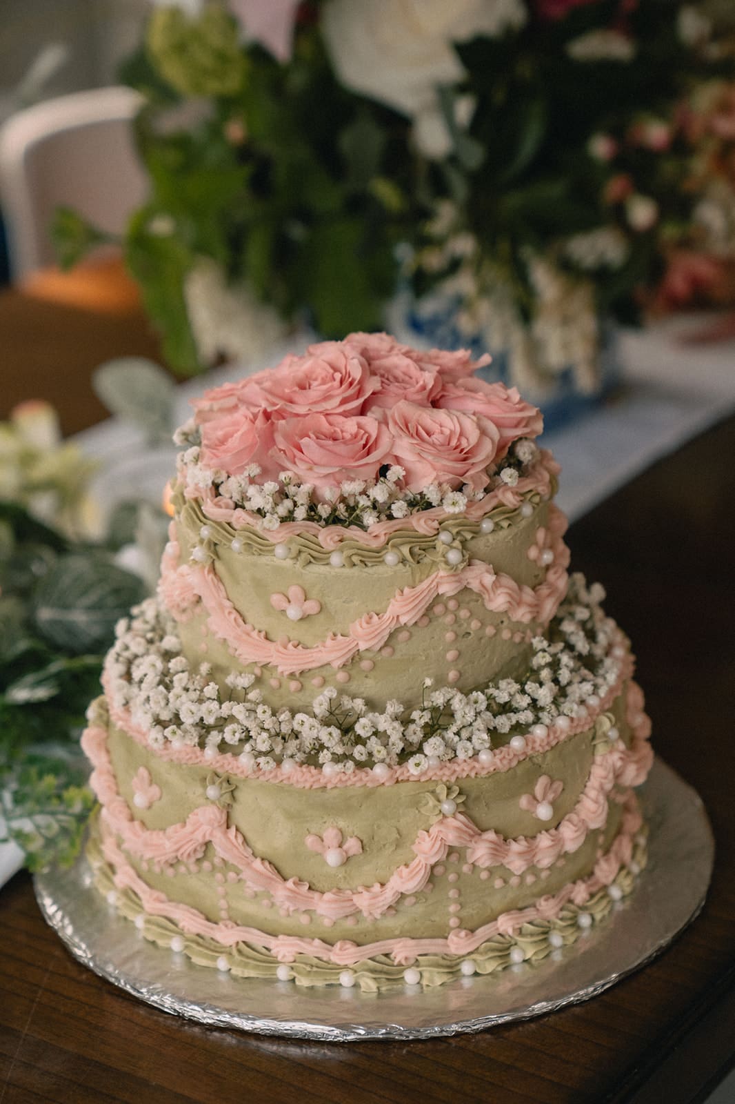 Vintage-style two-tier wedding cake with green frosting, pink piping, baby’s breath, and roses