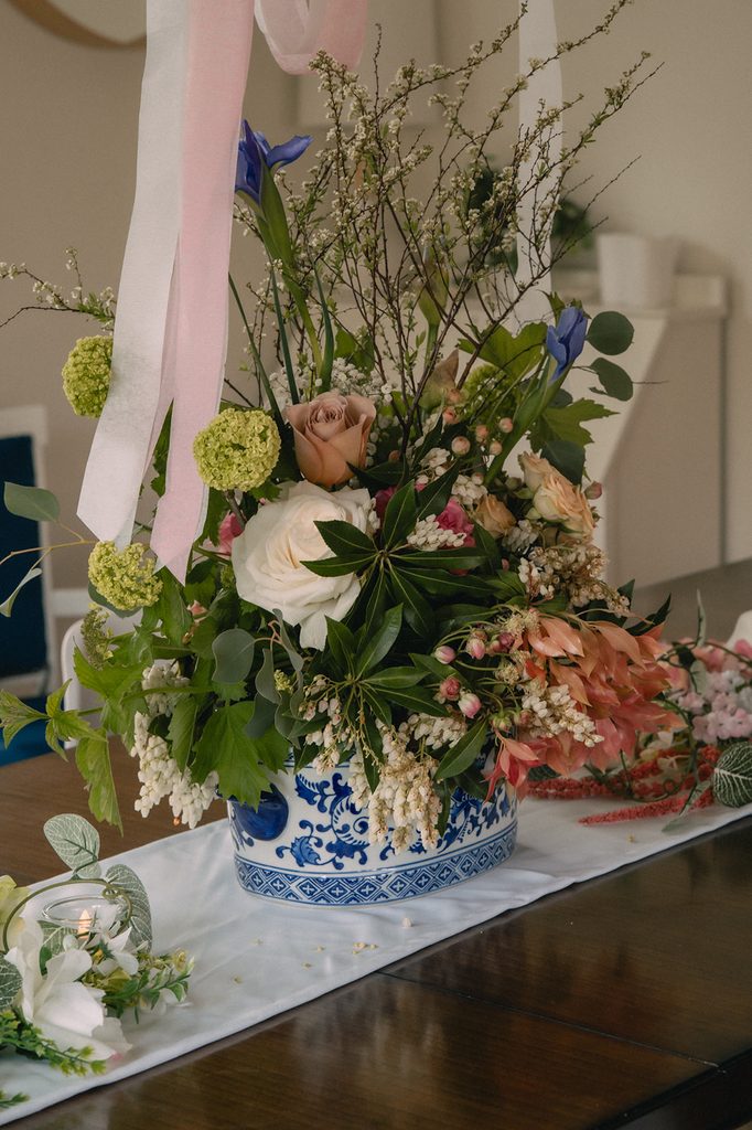 Colorful wedding centerpiece with pink roses, greenery, blue flowers, and a blue and white vase