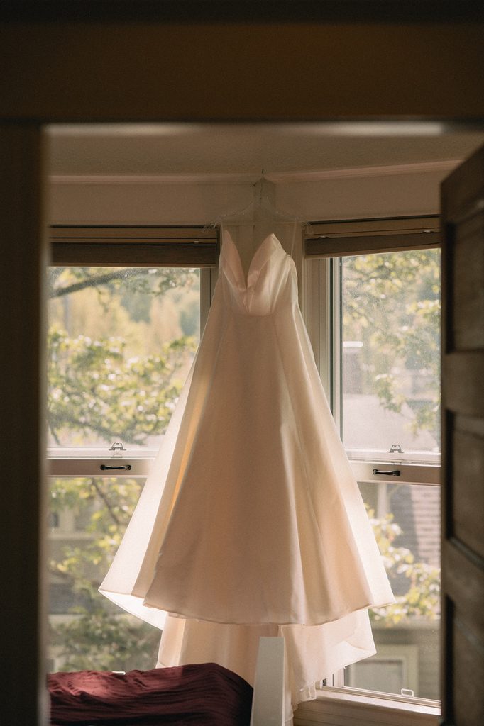 Brides dress hanging on the window as she gets ready for her Seattle micro wedding at an Airbnb. 